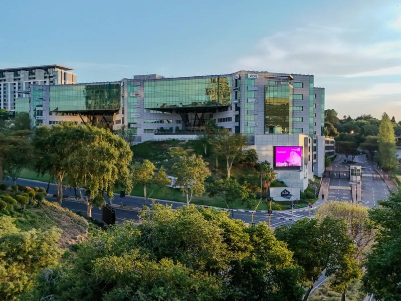 Aerial view of a modern commercial office complex featuring glass facade architecture, landscaped surroundings, and integrated digital signage.