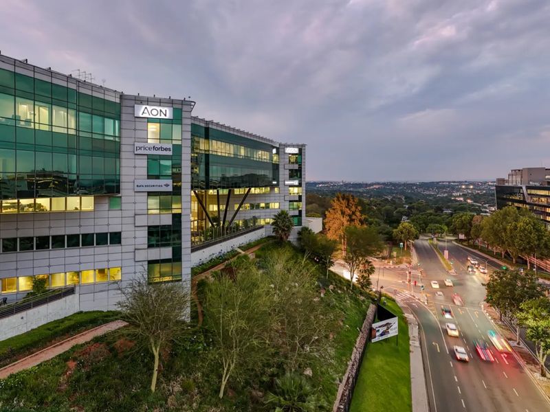 A professional aerial view of a modern commercial office building featuring a glass facade, prominent corporate signage, and landscaped grounds overlooking a busy urban street.