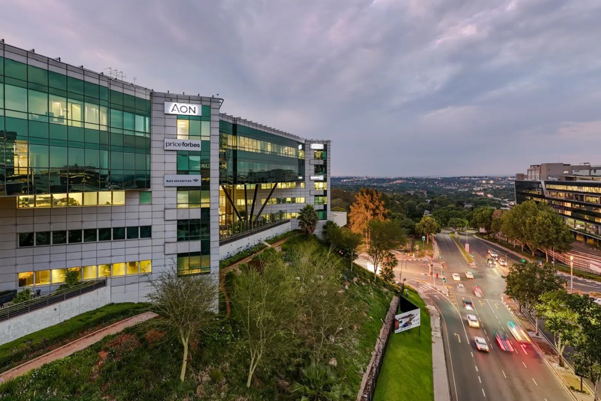 A professional aerial view of a modern commercial office building featuring a glass facade, prominent corporate signage, and landscaped grounds overlooking a busy urban street.