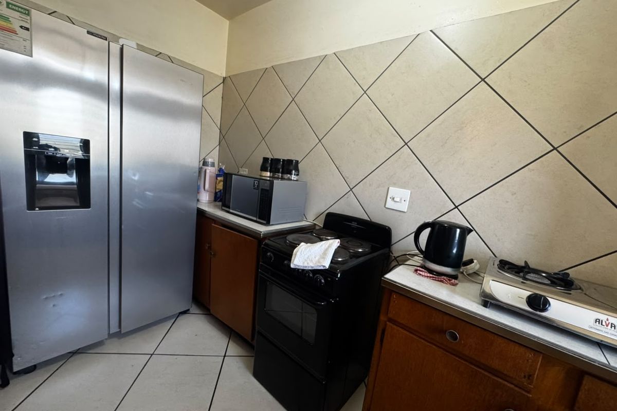 A functional kitchen featuring tiled flooring, a diamond-patterned backsplash, built-in cabinetry, and a freestanding stove with a large double-door refrigerator.