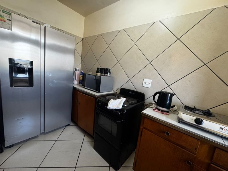 A functional kitchen featuring tiled flooring, a diamond-patterned backsplash, built-in cabinetry, and a freestanding stove with a large double-door refrigerator.