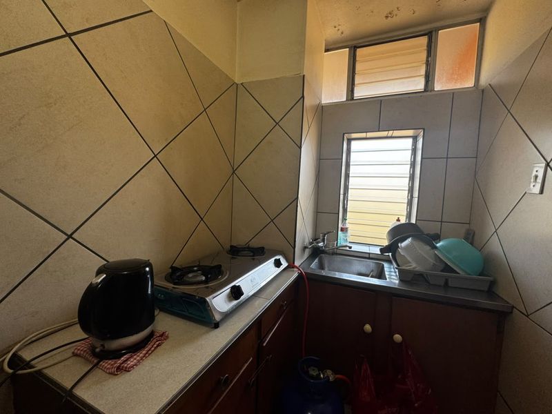 Compact kitchen area featuring a stainless steel sink, tiled splashback, and built-in cabinetry with a gas hob setup.
