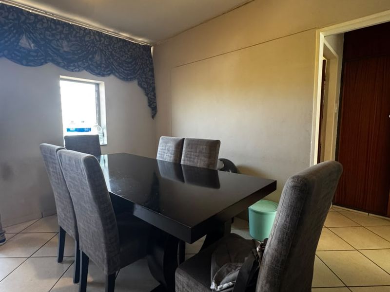 A dining area featuring ceramic floor tiles and a central pendant light, requiring cosmetic updates to the wall finishes.