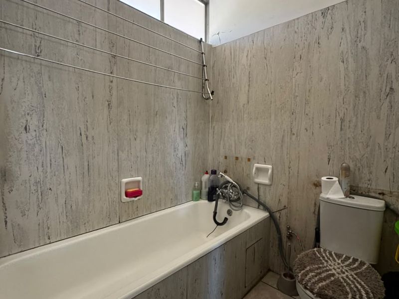 A dated bathroom featuring a bathtub, toilet, and tiled wall finishes. The space requires renovation to update the fixtures and address visible wall damage.