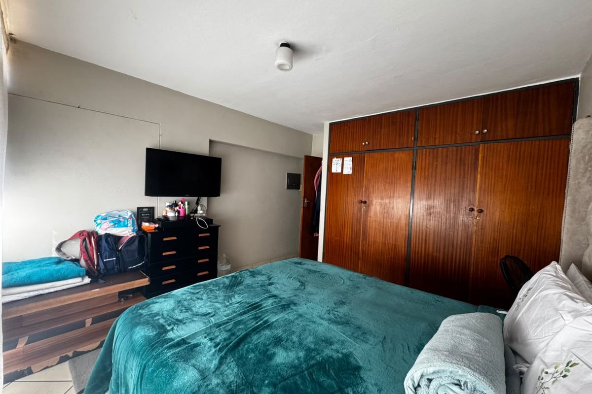 A bedroom featuring a large built-in wooden wardrobe with overhead storage compartments and a central ceiling light fixture.