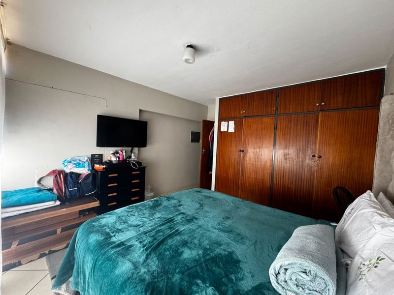 A bedroom featuring a large built-in wooden wardrobe with overhead storage compartments and a central ceiling light fixture.