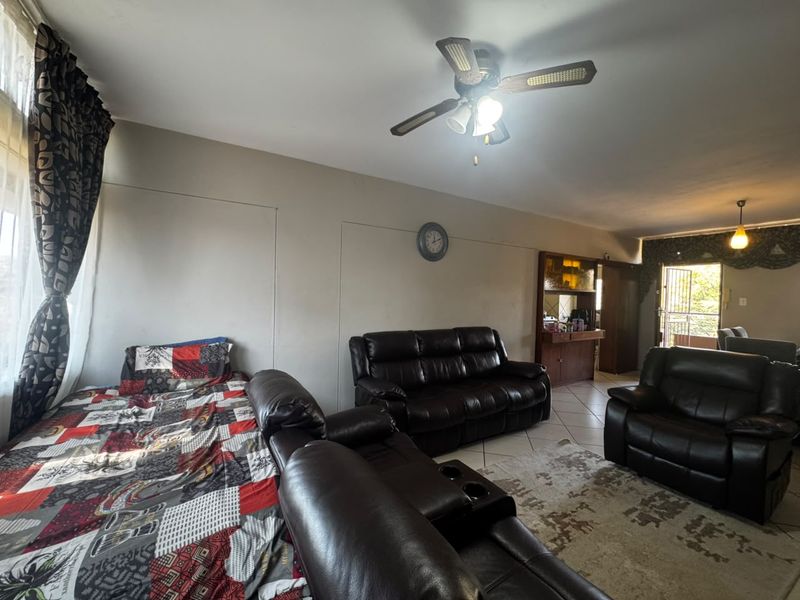 Spacious living area featuring tiled flooring, a ceiling fan, and a built-in display cabinet, with direct access to an outdoor area via a security gate.