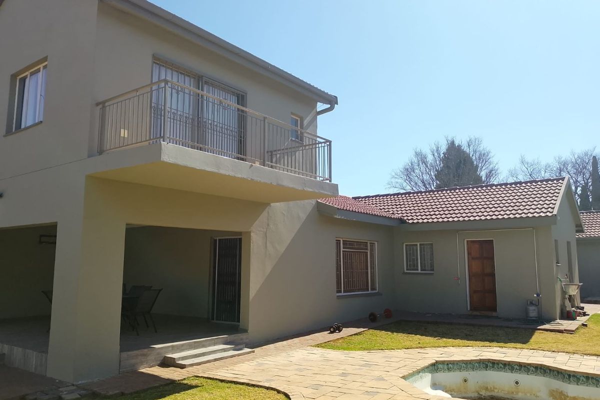 Rear view of a two-story house featuring a covered patio, upper-level balcony, and a swimming pool with paved surround.