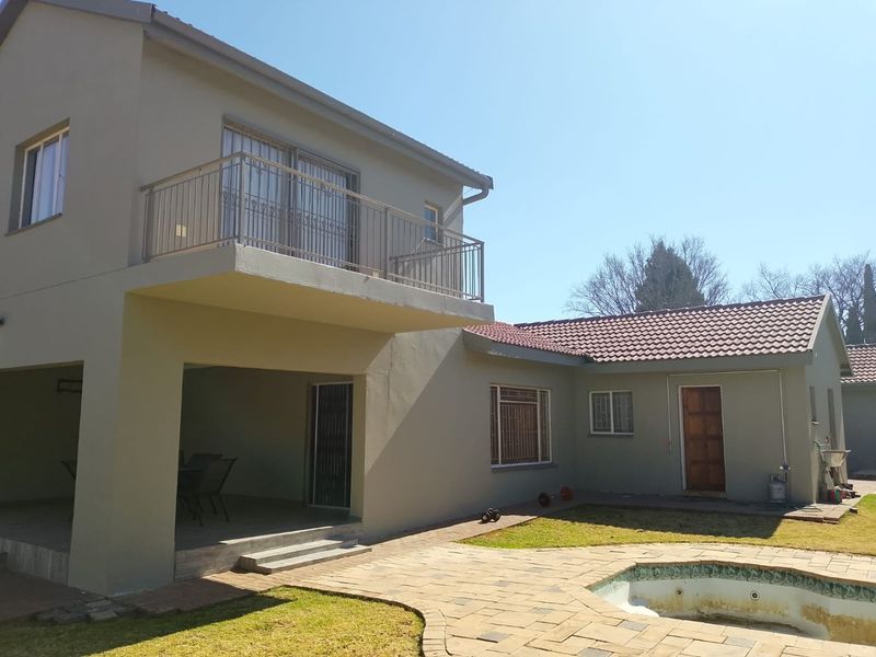 Rear view of a two-story house featuring a covered patio, upper-level balcony, and a swimming pool with paved surround.