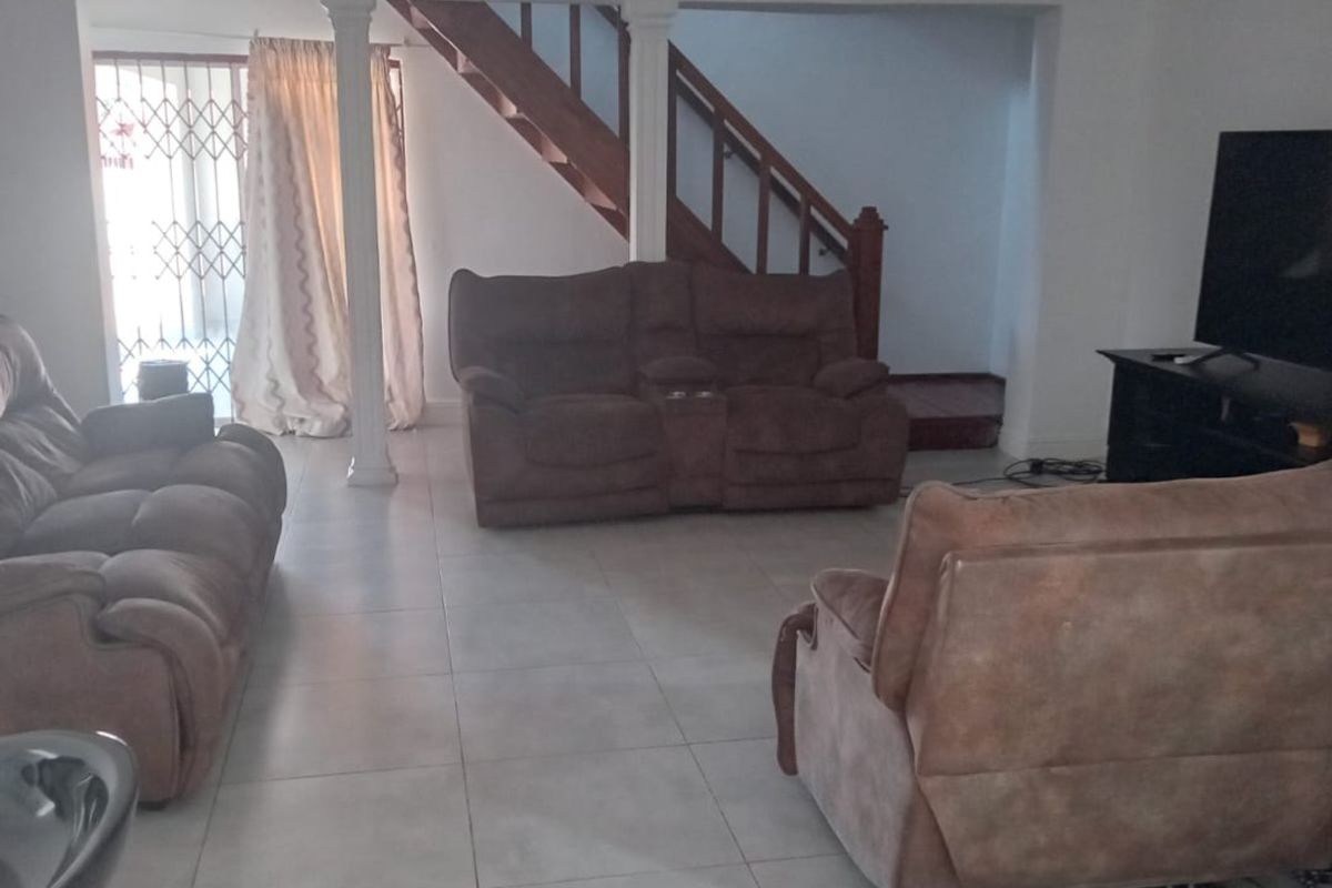 Spacious living area featuring tiled flooring, a wooden staircase, and decorative columns, providing an open layout with access to the exterior via a security gate.