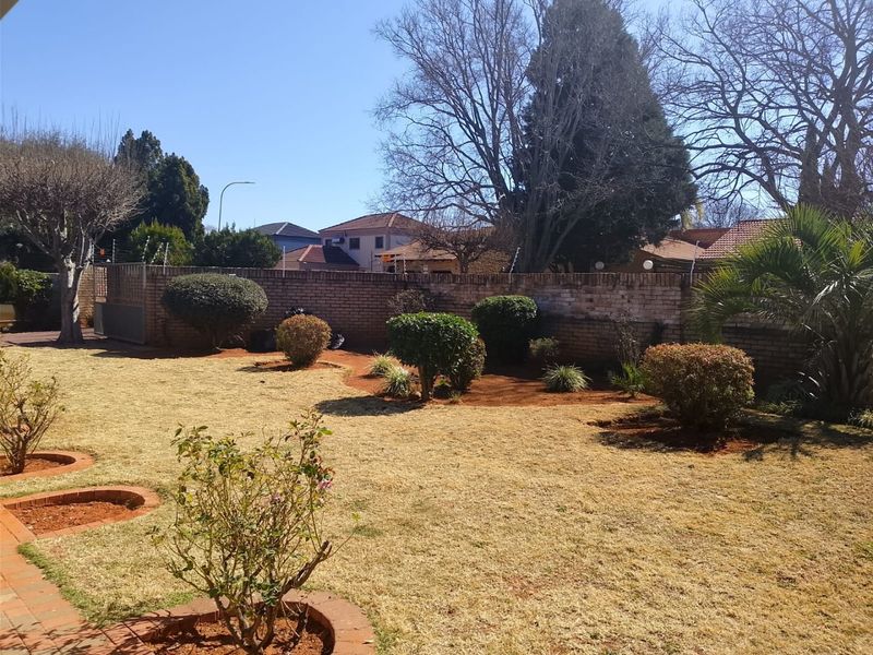 A spacious rear garden featuring a well-defined lawn, established shrubbery, and a secure brick boundary wall with integrated electric fencing.
