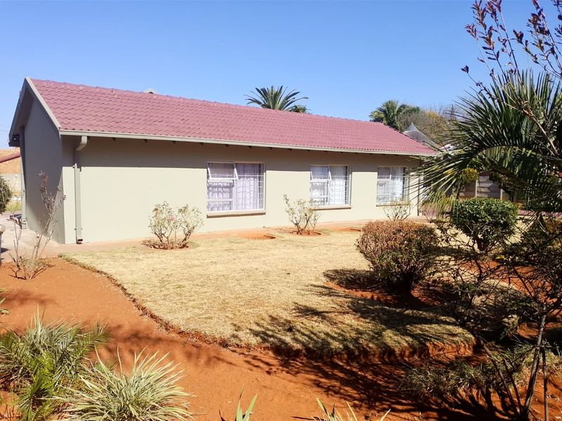 A view of the rear elevation of the house featuring a tiled roof, neutral exterior walls, and secure window frames overlooking a landscaped garden.