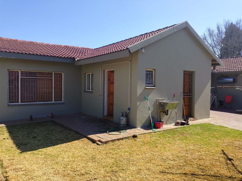 Rear view of the house featuring a paved patio area, external utility sink, and secure window bars.