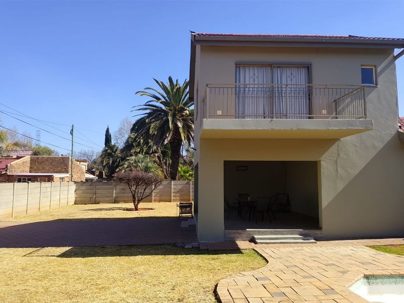 Rear view of the property featuring a covered patio, an upper-level balcony with metal railing, and a spacious backyard with paved areas.