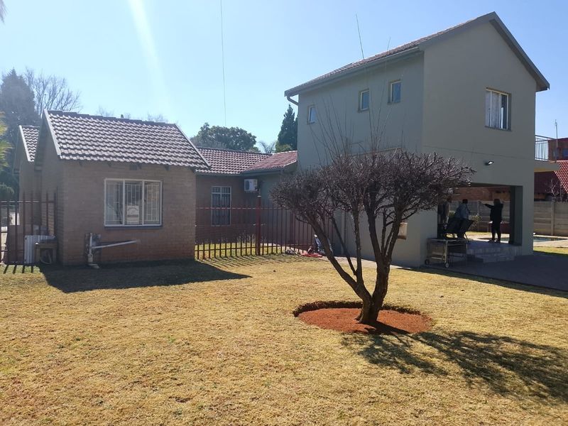 Rear view of the property featuring a brick and plastered facade, tiled roof, and a covered patio area overlooking the garden.