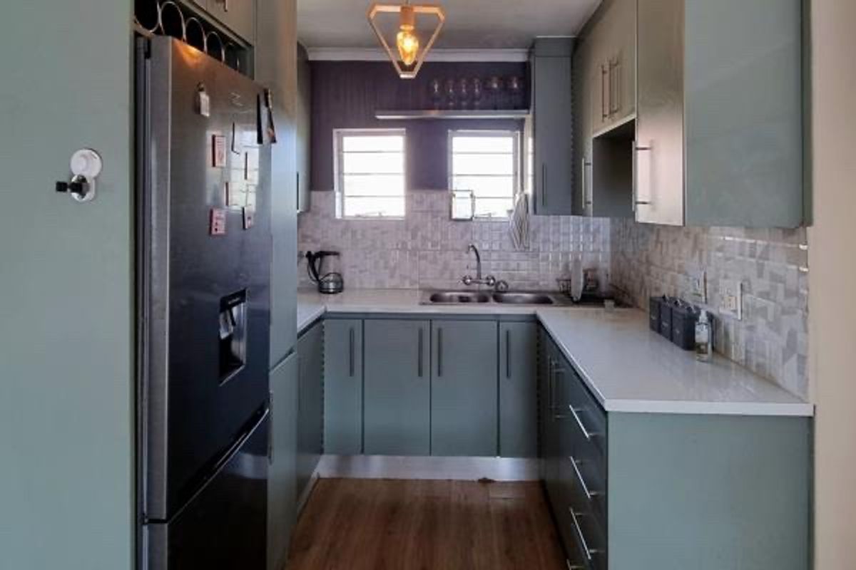 A modern, U-shaped kitchen featuring sage green cabinetry, white laminate countertops, a tiled backsplash, and integrated wine storage.