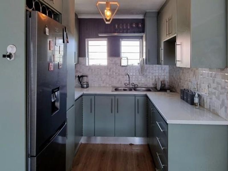 A modern, U-shaped kitchen featuring sage green cabinetry, white laminate countertops, a tiled backsplash, and integrated wine storage.