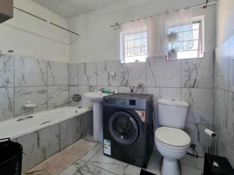 A functional bathroom featuring marble-look wall tiles, a bathtub, a pedestal basin, and a toilet, requiring some cosmetic attention to the ceiling and walls.