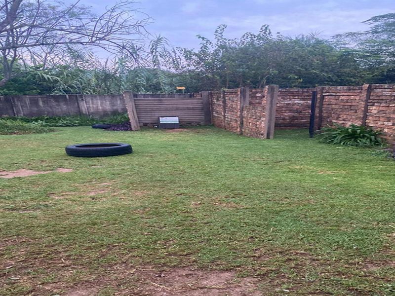A private backyard area featuring a lawn enclosed by brick and concrete boundary walls.