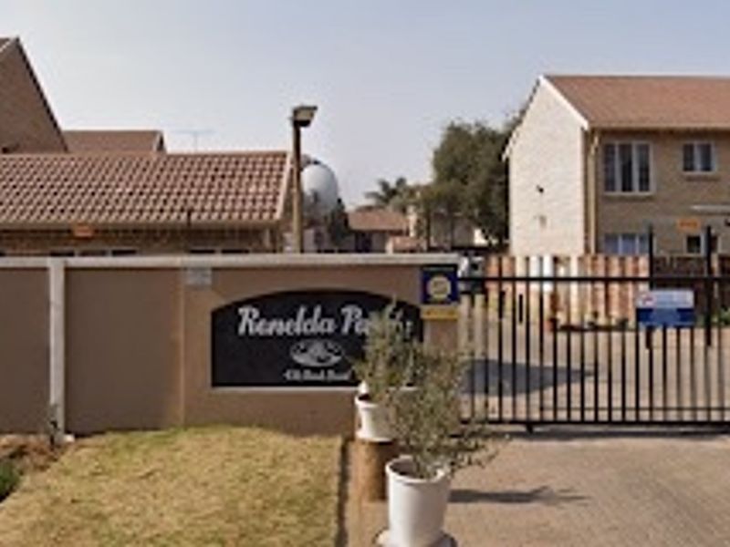 Front entrance view of Renelda Park apartment complex featuring a secure gated access point, perimeter walling with electric fencing, and brick-faced residential buildings.