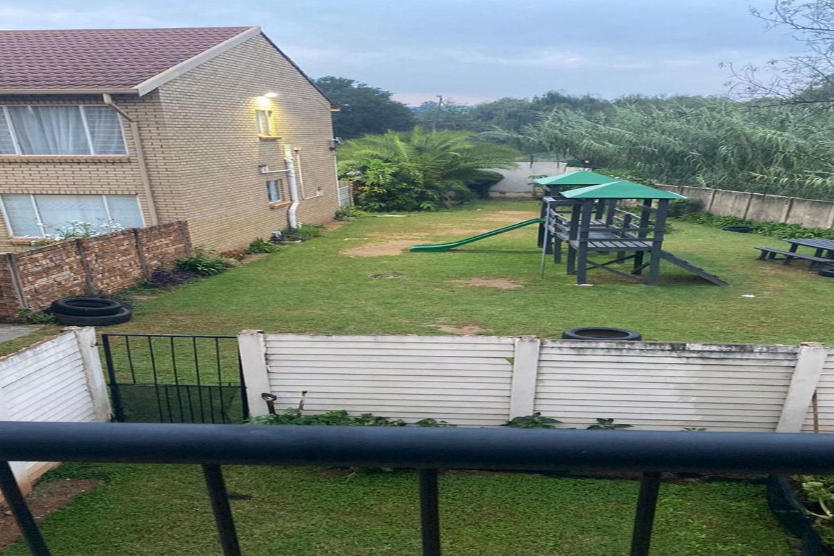 View of the rear garden area featuring a brick apartment building facade, perimeter walling, and a shared lawn space.