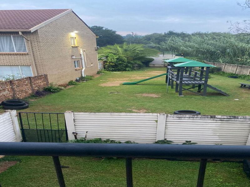 View of the rear garden area featuring a brick apartment building facade, perimeter walling, and a shared lawn space.