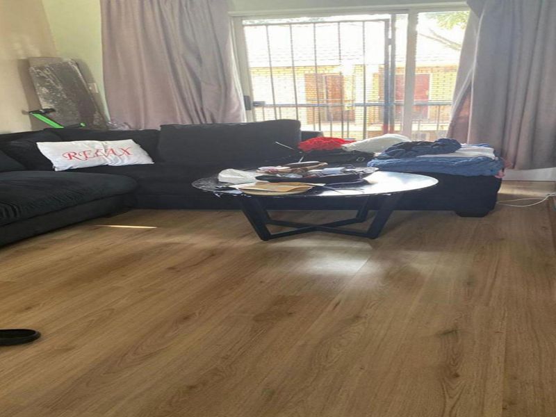 A living room featuring laminate flooring and a sliding glass door with an integrated security gate, providing access to the exterior.