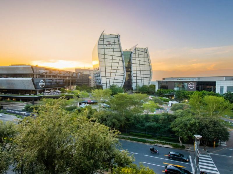 An elevated aerial view of a modern commercial office park featuring contemporary architecture, landscaped green spaces, and surrounding road infrastructure at sunset.