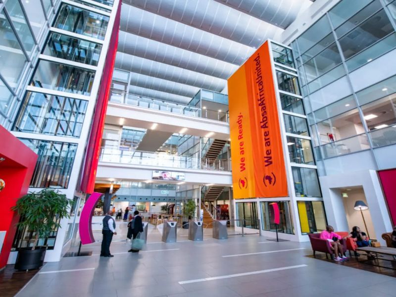 Spacious modern commercial atrium featuring high ceilings, glass elevator shafts, security turnstiles, and large windows providing ample natural light.