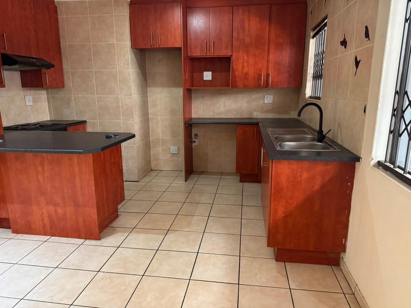 A functional kitchen featuring wood-look cabinetry, dark countertops, a double sink, and tiled surfaces throughout, offering a practical layout for daily use.