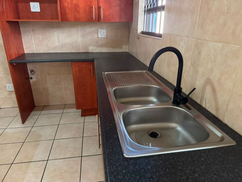 A functional kitchen area featuring laminate cabinetry, dark countertops, a double bowl sink with a modern black mixer tap, and tiled finishes.