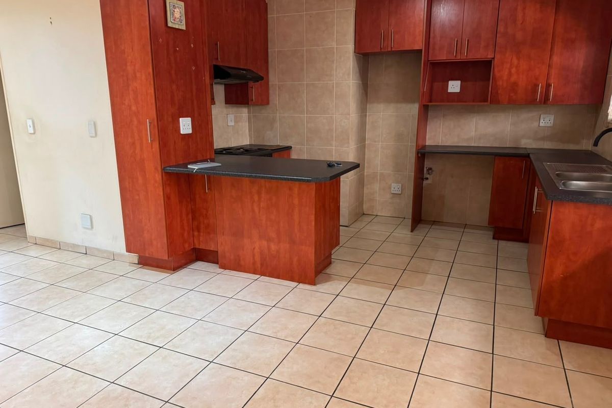 A functional kitchen featuring cherry-toned built-in cabinetry, dark laminate countertops, tiled backsplash, and ceramic floor tiles in an open-plan layout.