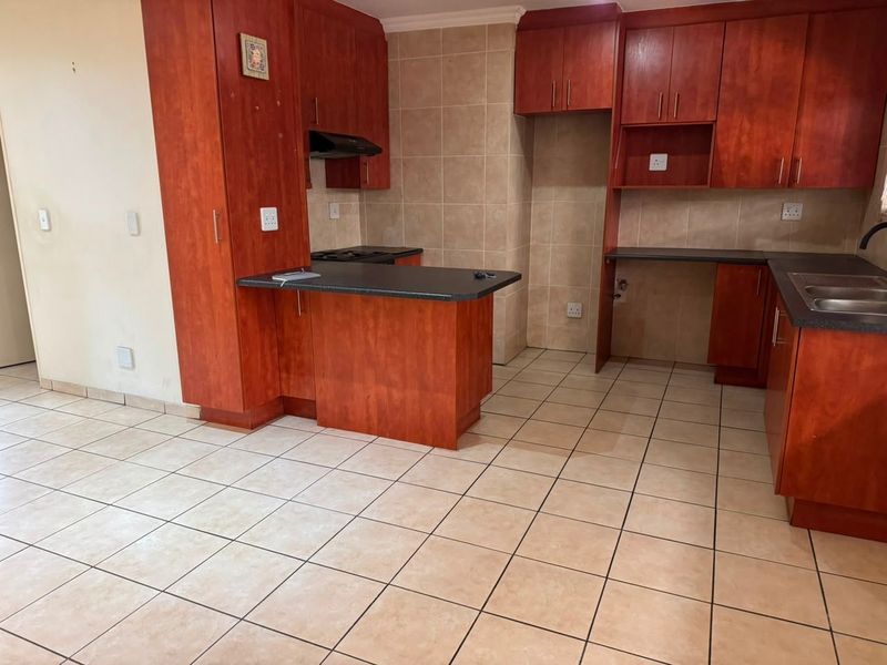 A functional kitchen featuring cherry-toned built-in cabinetry, dark laminate countertops, tiled backsplash, and ceramic floor tiles in an open-plan layout.