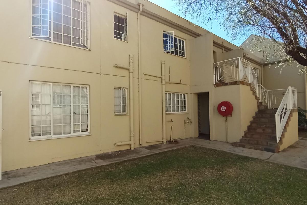 Rear exterior view of the apartment building featuring an external staircase, metal balustrades, and visible exterior plumbing infrastructure.