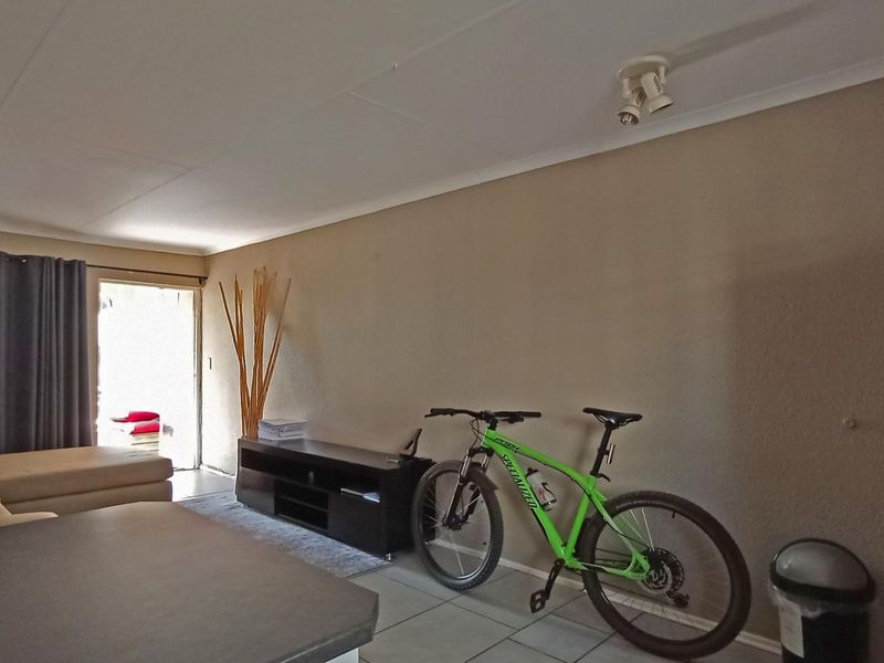 A living room area featuring tiled flooring and ceiling-mounted spotlights, with direct access to an outdoor space through a sliding door.