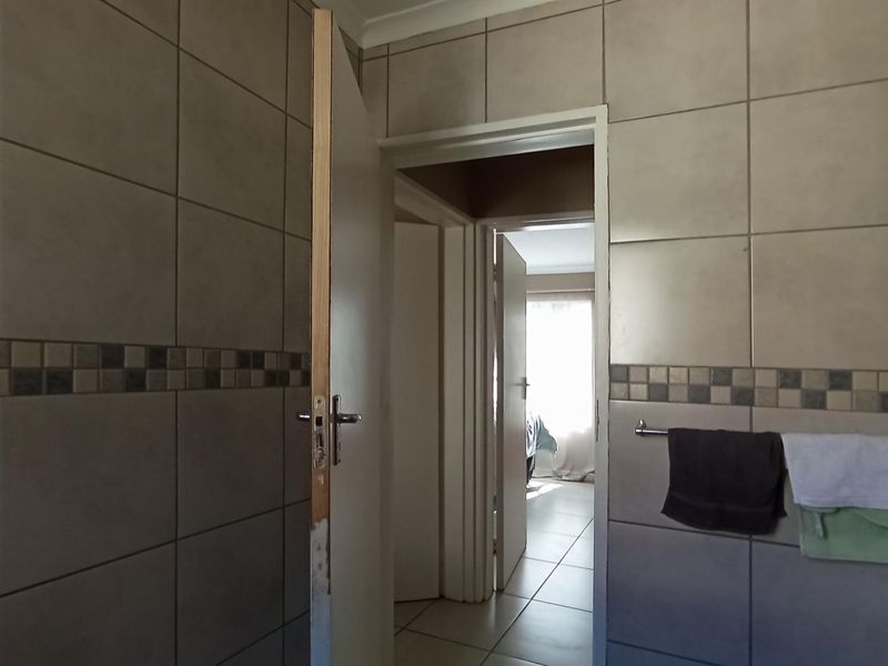A bathroom interior featuring neutral ceramic wall tiles with a decorative border and a functional towel rail, leading into a hallway.