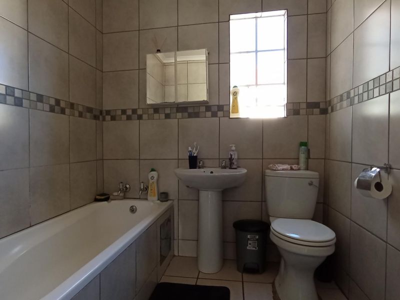 A functional bathroom featuring a bathtub, pedestal basin, and toilet, finished with neutral wall and floor tiles.