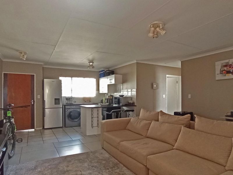 Open-plan living area featuring a functional kitchen with island, tiled flooring, and neutral wall tones, providing a versatile space for daily living.