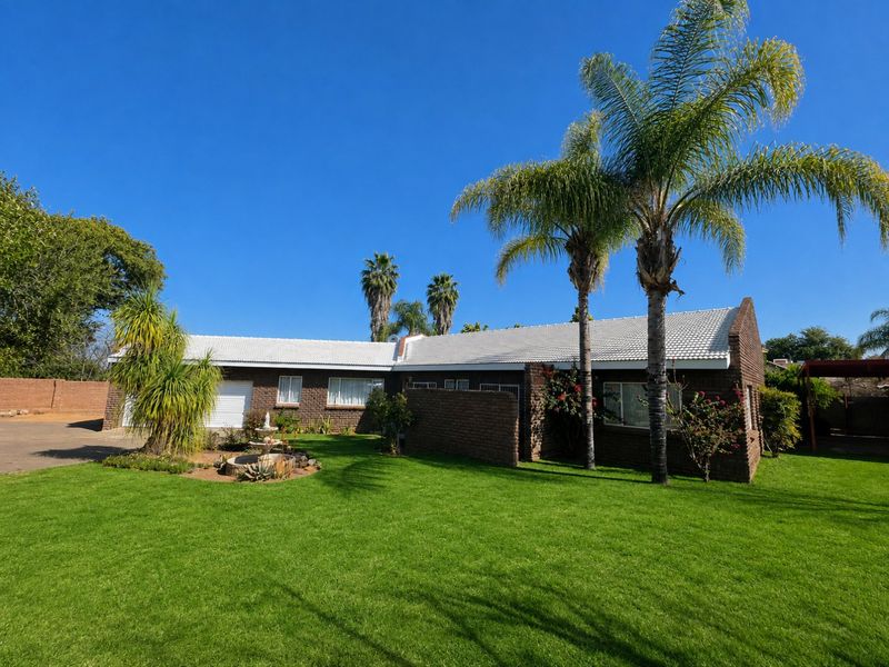 A well-maintained single-story brick home featuring a tiled roof, attached garage, and a spacious front lawn with established palm trees.