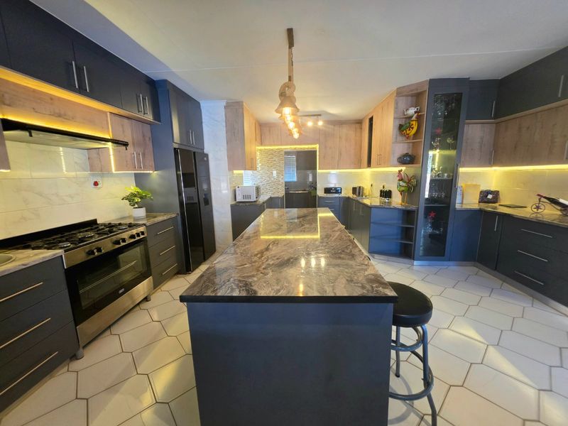 Modern kitchen featuring a large central island, stone countertops, dark cabinetry with wood accents, integrated lighting, and stylish hexagonal floor tiles.