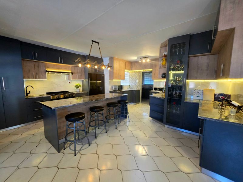 Modern, well-appointed kitchen featuring a large central island, stone countertops, extensive built-in cabinetry, and integrated lighting, finished with stylish hexagonal floor tiles.