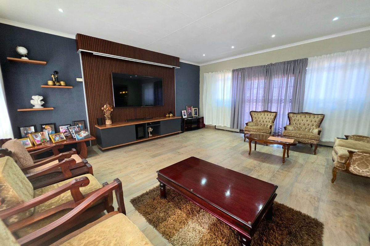 Spacious living room featuring modern timber-look floor tiles, a stylish wood-paneled feature wall with integrated media console, and large sliding doors for natural light.