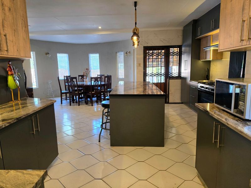 Spacious open-plan kitchen and dining area featuring modern dark cabinetry, stone countertops, a central island, and tiled flooring throughout.