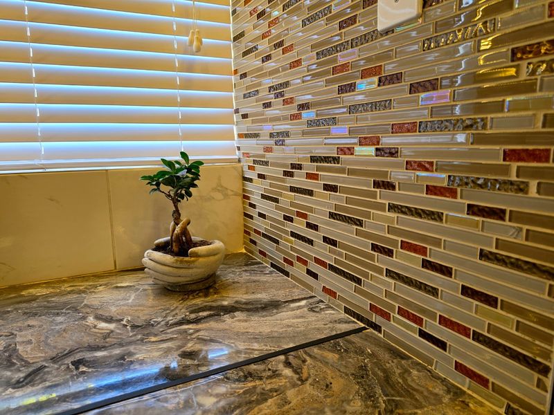 Close-up view of a kitchen workspace featuring a decorative mosaic tile backsplash and a marble-effect countertop with integrated venetian blinds.