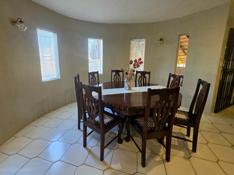 A dining room featuring tiled flooring, curved walls, and multiple windows with vertical blinds, providing a bright and functional space for meals.