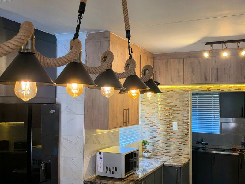 Modern kitchen featuring wood-grain and dark cabinetry, stone countertops, mosaic tile backsplash, and decorative rope pendant lighting.