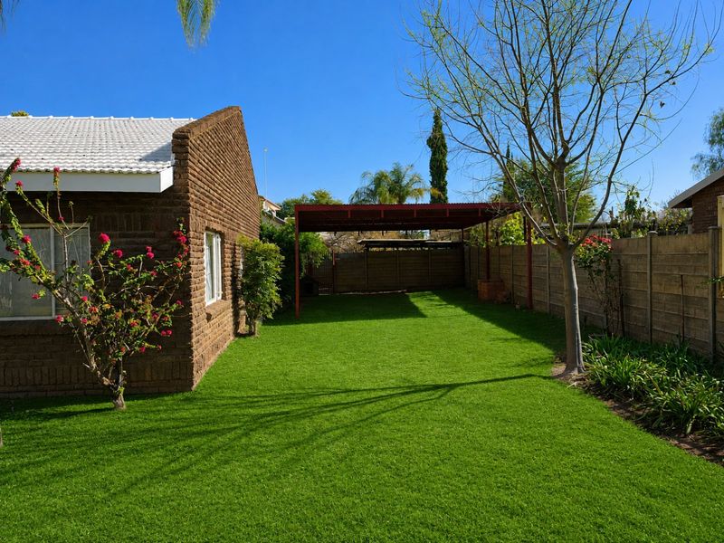 A well-maintained rear garden featuring a neat lawn, brick exterior wall, and a covered metal carport structure.