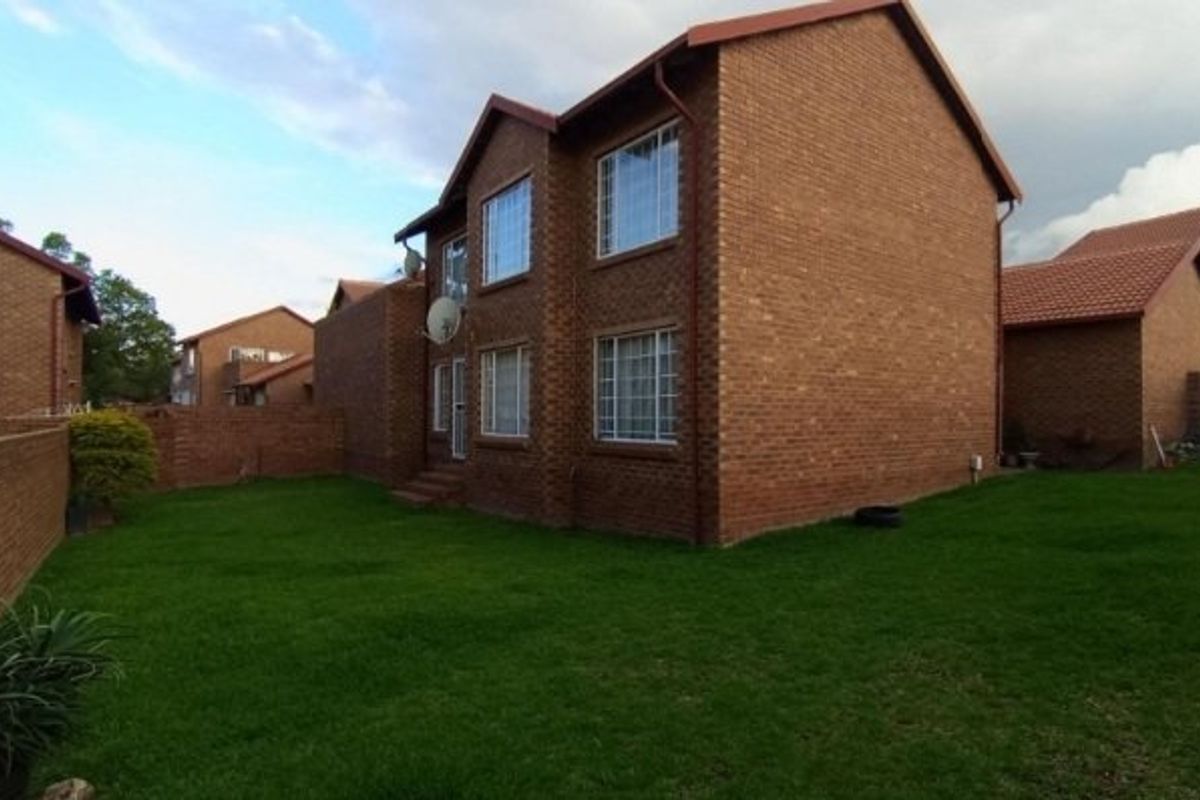 Rear view of a double-story face brick apartment building featuring a private lawn area and secure boundary walling.