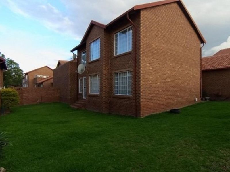 Rear view of a double-story face brick apartment building featuring a private lawn area and secure boundary walling.