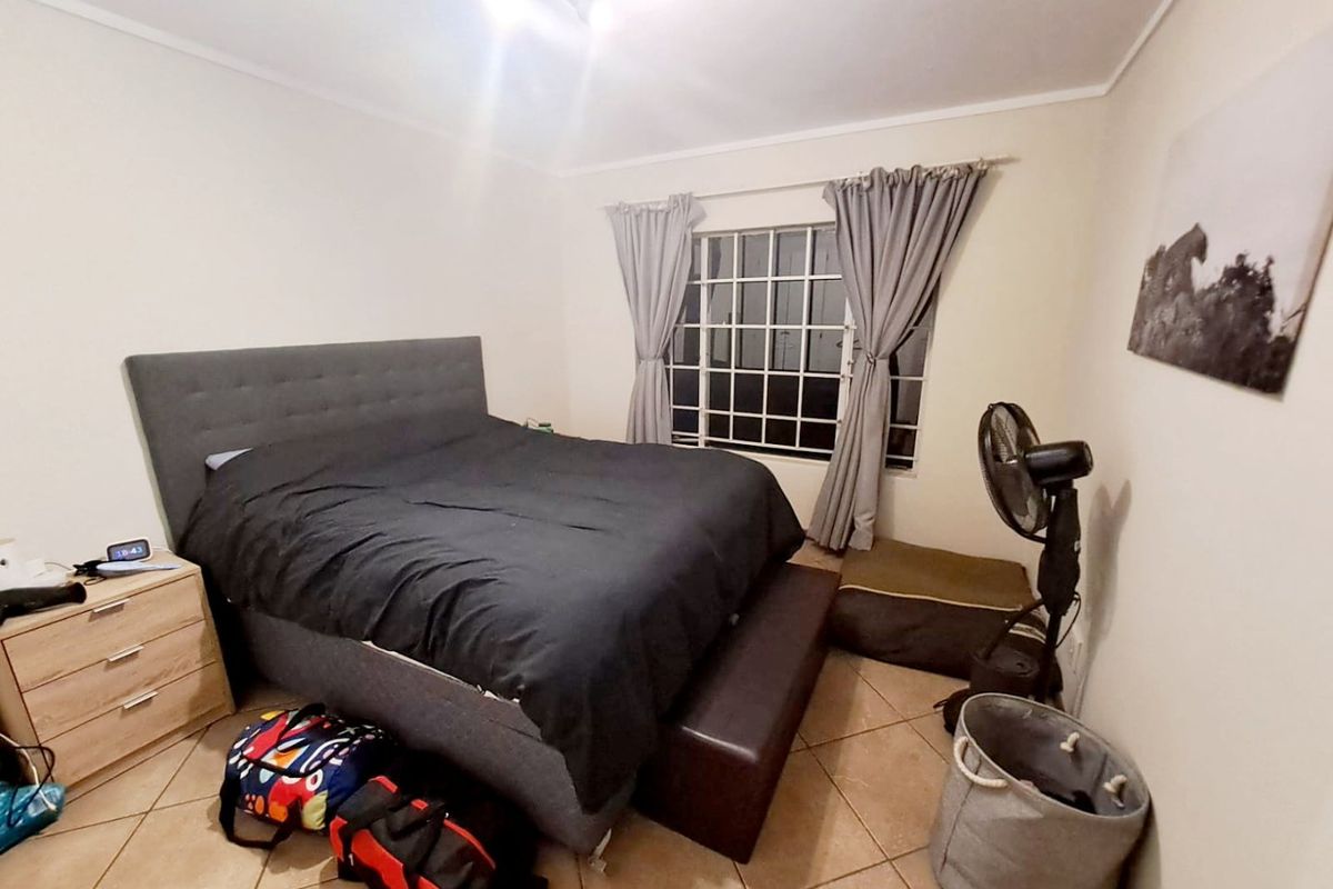 A functional bedroom featuring tiled flooring and a window fitted with security bars.